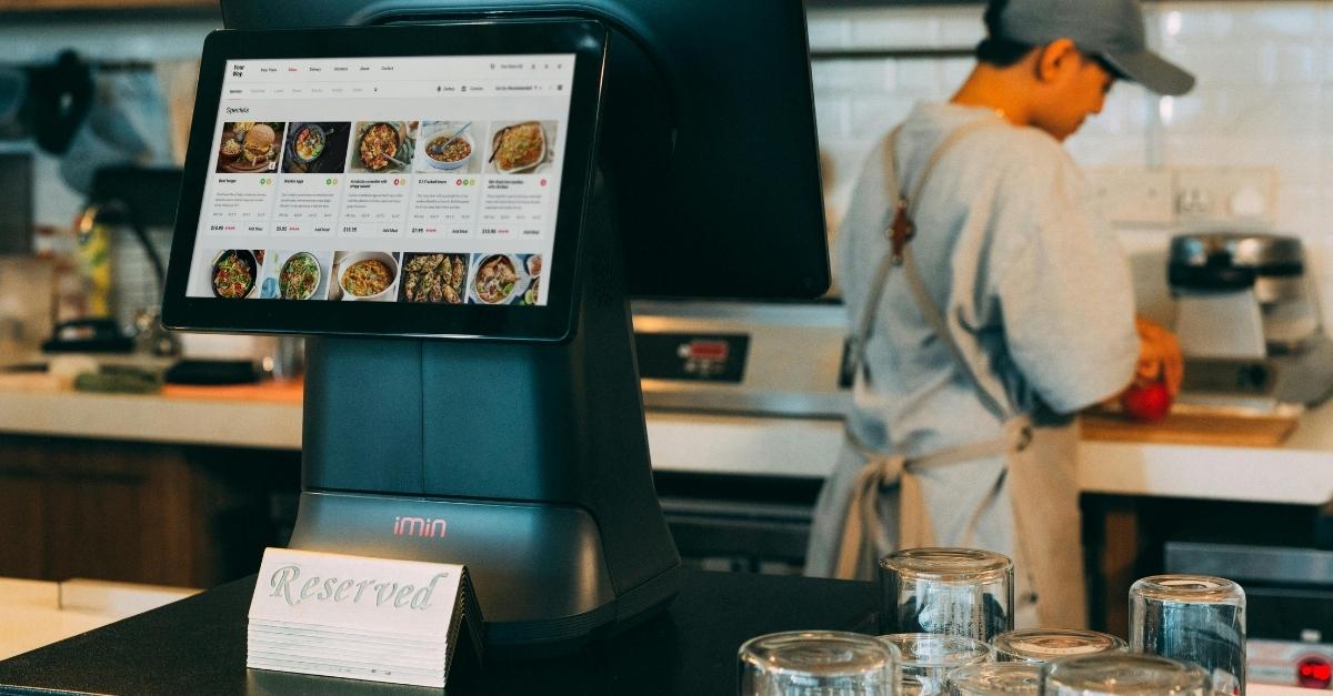 A Man Cleaning Kitchen Tools at the back and A Reservation Standee At His Back besides POS Hardware | Condor PH