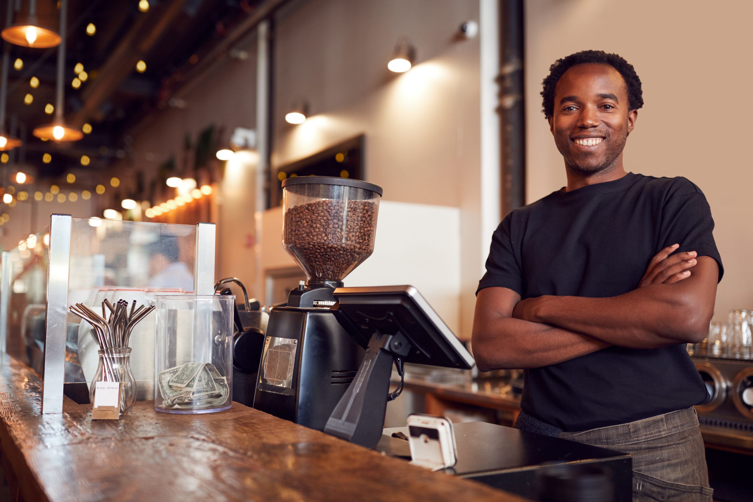 Male Coffee Shop Owner Standing At Sales Desk
