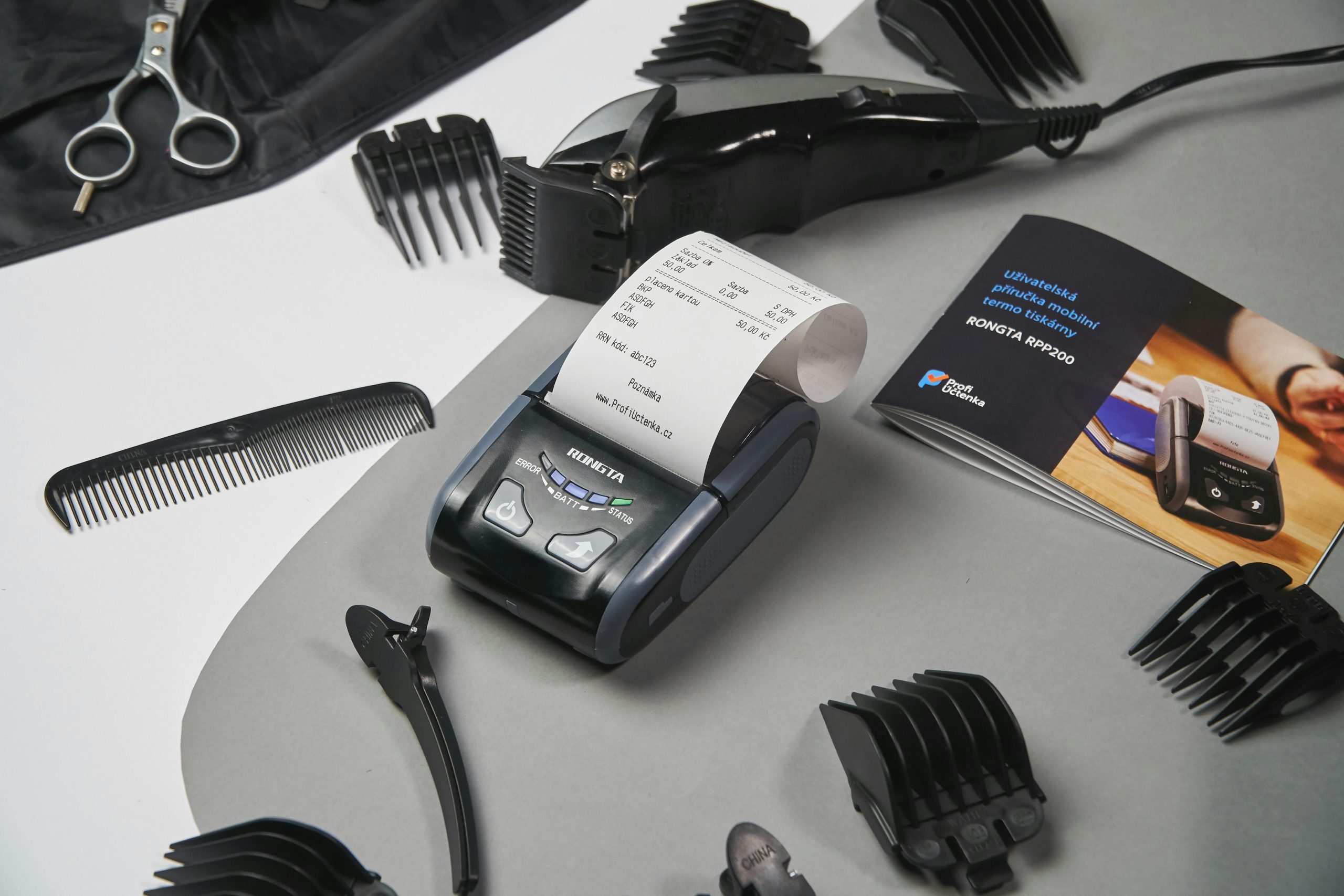 A portable thermal receipt printer on a salon workstation surrounded by haircutting tools and a manual guide | Condor PH